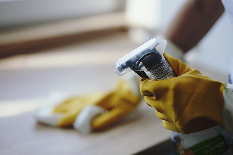 Hands in yellow gloves with a spray bottle and a cleaning cloth